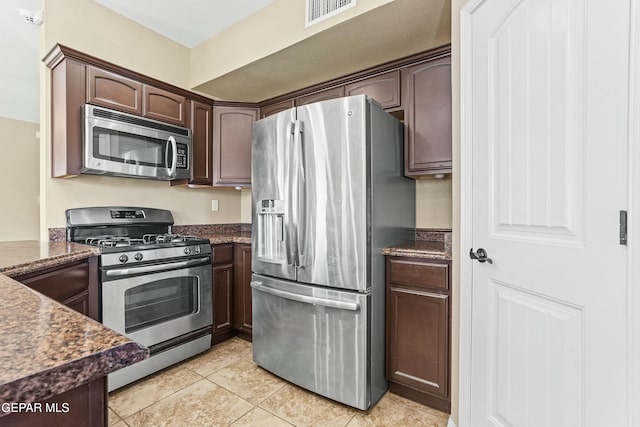 kitchen featuring stainless steel appliances, dark stone countertops, light tile patterned floors, and dark brown cabinetry