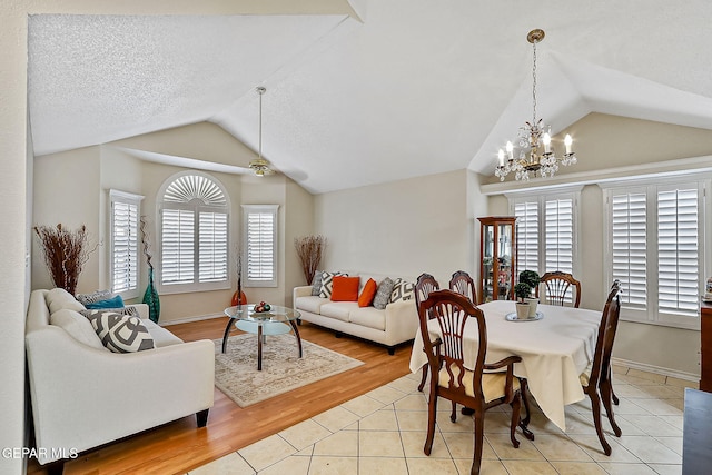 dining room with light tile patterned floors, vaulted ceiling, ceiling fan with notable chandelier, and baseboards