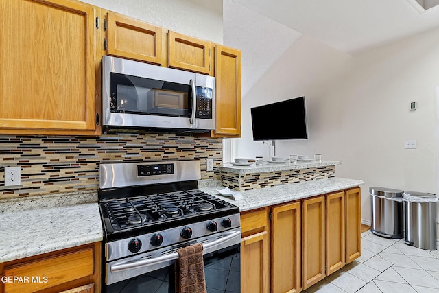 kitchen with light tile patterned floors, decorative backsplash, appliances with stainless steel finishes, vaulted ceiling, and light stone countertops