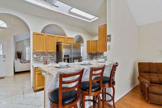 kitchen with stainless steel fridge, a peninsula, a breakfast bar area, and light stone countertops