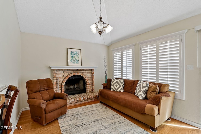 living room with light wood finished floors, an inviting chandelier, a brick fireplace, a textured ceiling, and baseboards