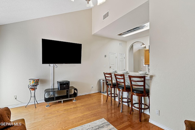 living area featuring arched walkways, light wood finished floors, lofted ceiling, visible vents, and baseboards