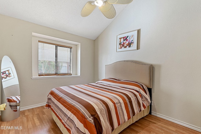 bedroom featuring light wood-style floors, a ceiling fan, vaulted ceiling, a textured ceiling, and baseboards