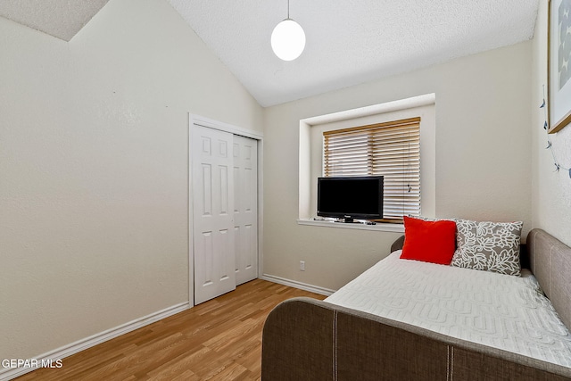 bedroom with a closet, vaulted ceiling, a textured ceiling, wood finished floors, and baseboards