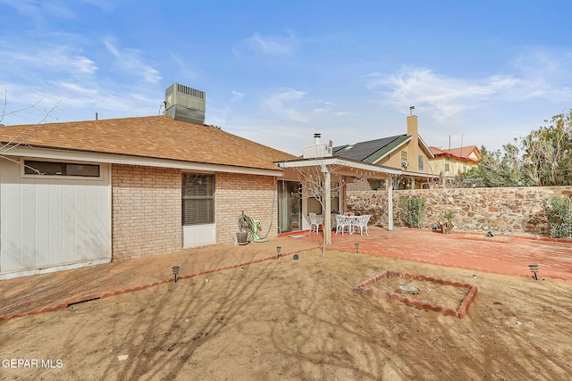 rear view of property featuring a patio, brick siding, roof with shingles, and fence