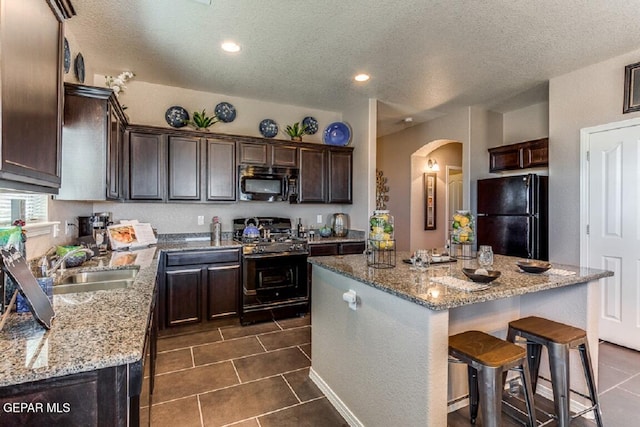 kitchen with dark tile patterned floors, a center island, light stone counters, and black appliances