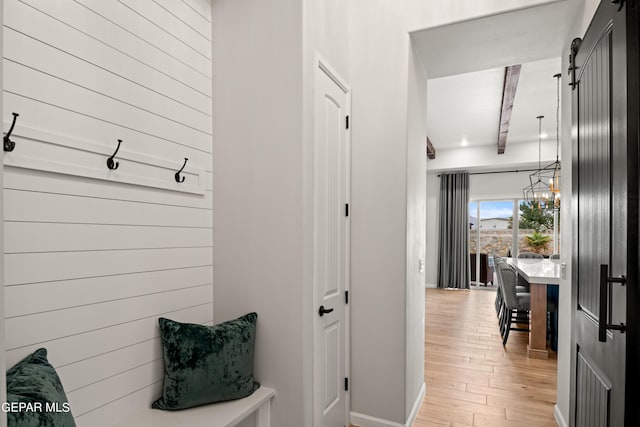 mudroom featuring a chandelier, light wood-type flooring, beam ceiling, and wooden walls