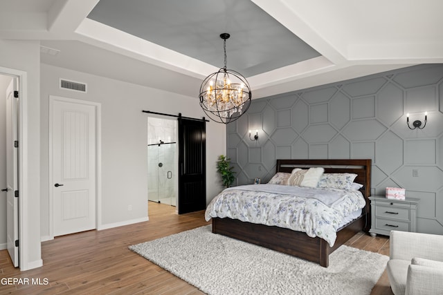 bedroom with light wood finished floors, visible vents, a barn door, an accent wall, and baseboards