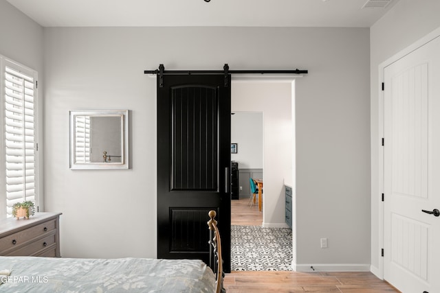 bedroom featuring visible vents, light wood-style flooring, baseboards, and a barn door