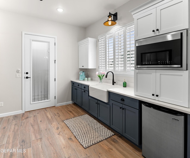 kitchen with a sink, white cabinets, light countertops, and gray cabinetry