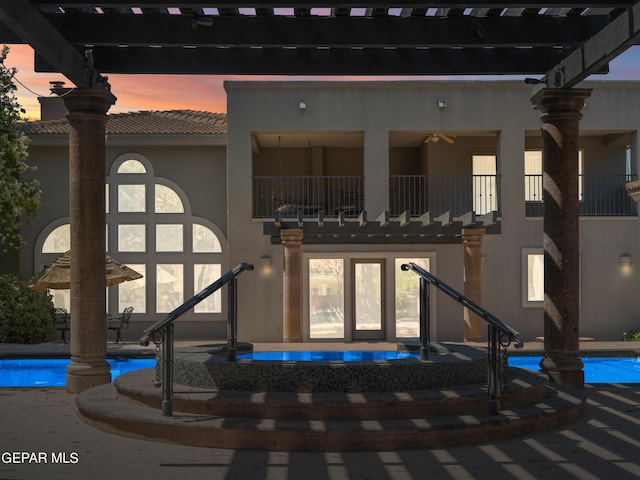 rear view of house featuring stucco siding, a patio area, a balcony, an outdoor pool, and a tiled roof