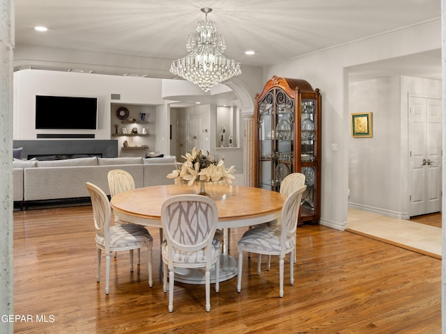 dining space with arched walkways, a chandelier, visible vents, baseboards, and light wood finished floors