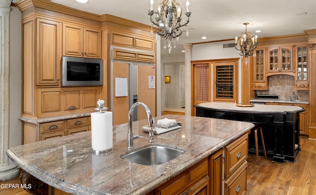 kitchen with an island with sink, glass insert cabinets, built in appliances, light stone countertops, and an inviting chandelier