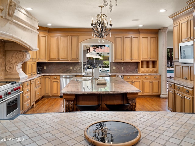 kitchen with stainless steel appliances, light stone counters, an island with sink, and a sink