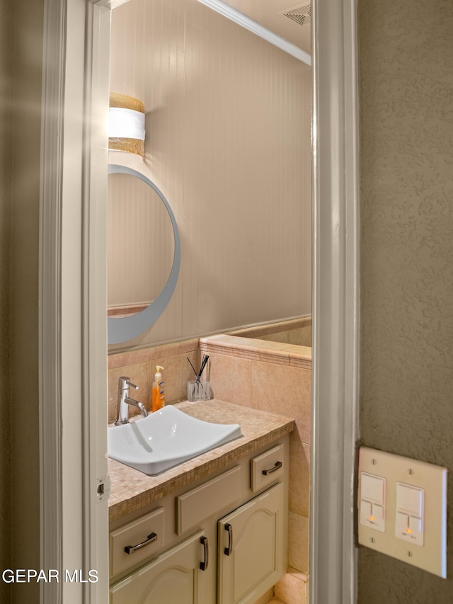 bathroom featuring visible vents, ornamental molding, tile walls, and vanity