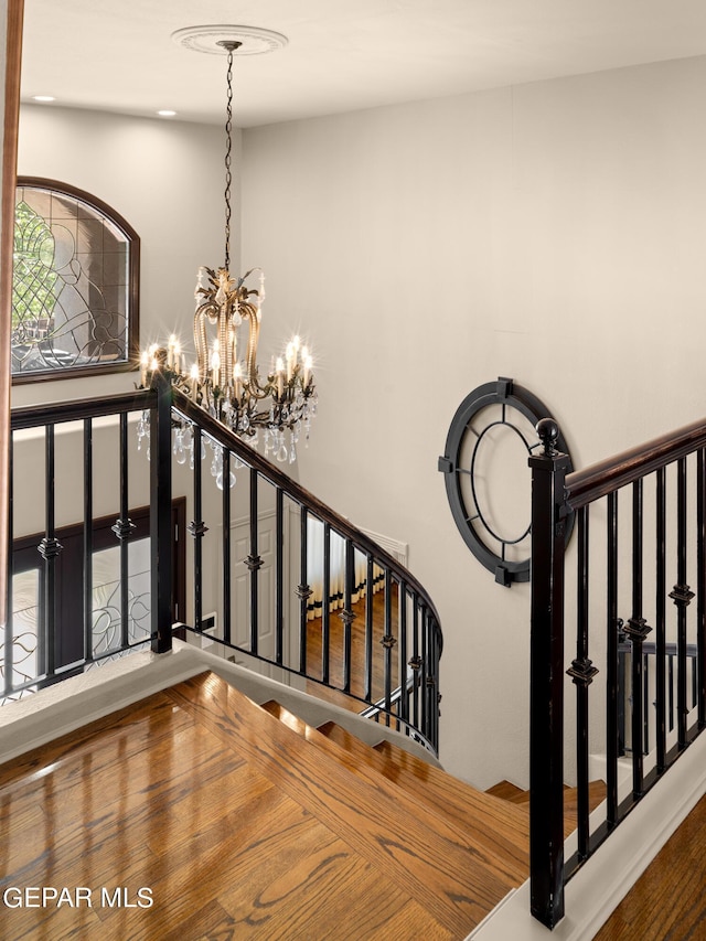 staircase featuring wood finished floors and an inviting chandelier