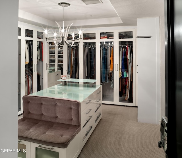 walk in closet with a tray ceiling, a chandelier, and light colored carpet