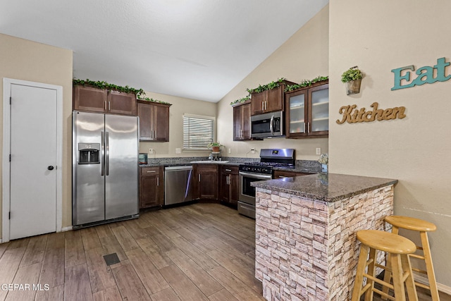 kitchen featuring appliances with stainless steel finishes, lofted ceiling, a kitchen bar, dark brown cabinetry, and kitchen peninsula