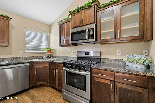 kitchen with lofted ceiling, stainless steel appliances, sink, and dark stone counters