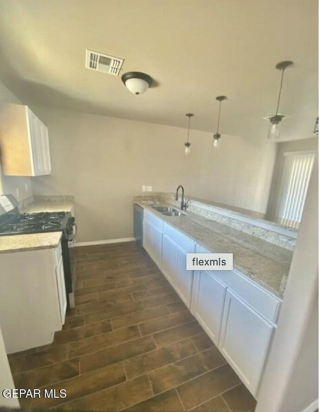 kitchen featuring hanging light fixtures, sink, stainless steel range with gas stovetop, and white cabinets