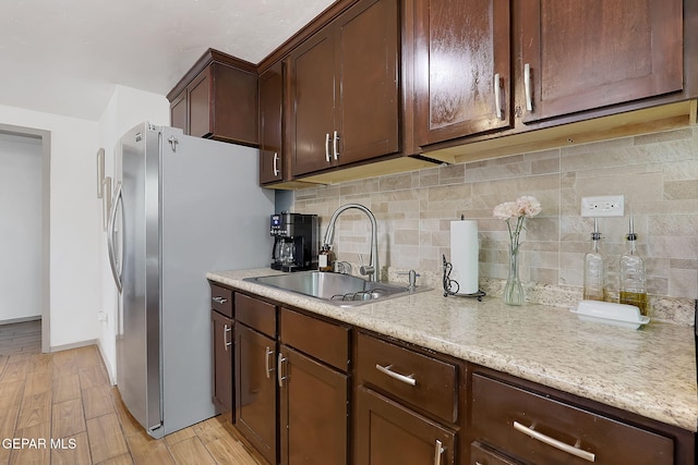 kitchen featuring sink, stainless steel fridge, dark brown cabinetry, decorative backsplash, and light wood-type flooring