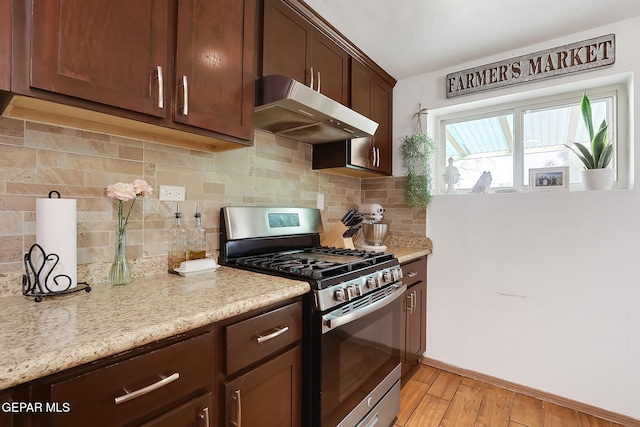 kitchen with stainless steel range with gas cooktop, light stone counters, light hardwood / wood-style floors, and decorative backsplash