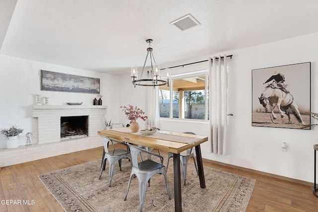 dining area featuring wood-type flooring, a brick fireplace, a chandelier, and a textured ceiling