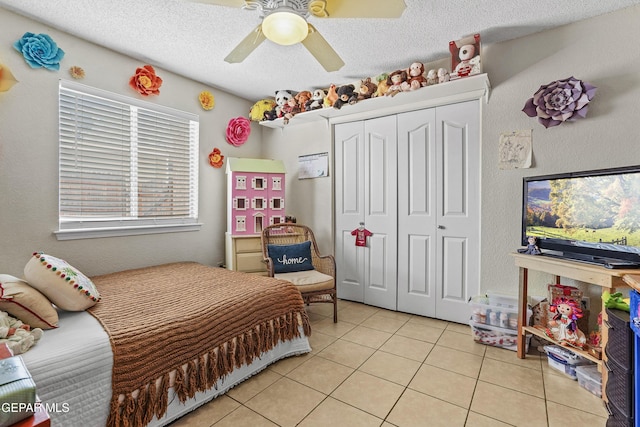 bedroom featuring a textured ceiling, a closet, ceiling fan, and light tile patterned flooring