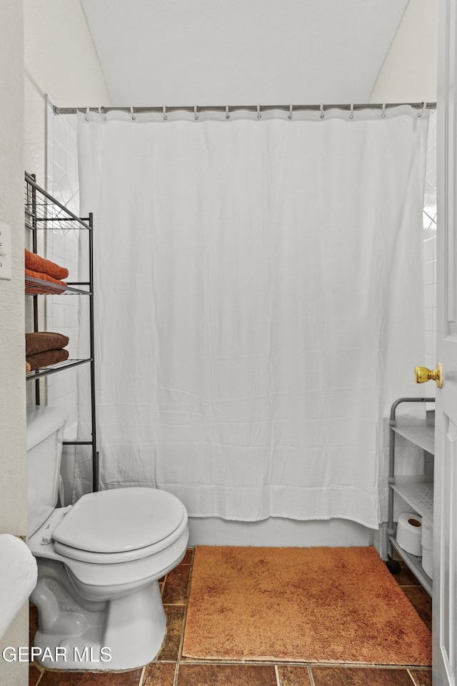 bathroom with tile patterned floors, shower / bath combo with shower curtain, and toilet