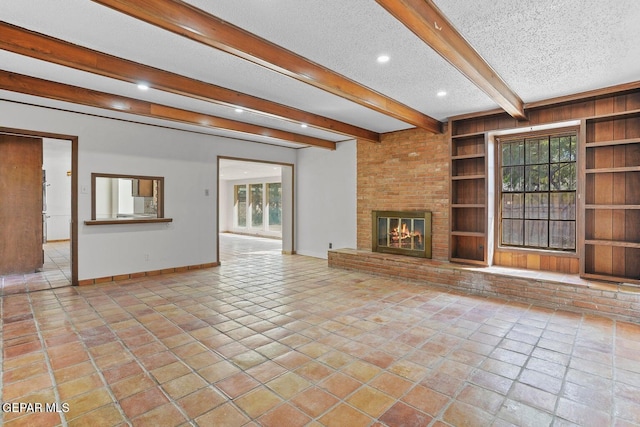 unfurnished living room featuring built in features, beamed ceiling, a textured ceiling, a brick fireplace, and baseboards