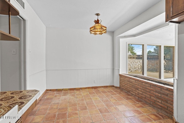 unfurnished dining area with brick wall, wainscoting, and visible vents