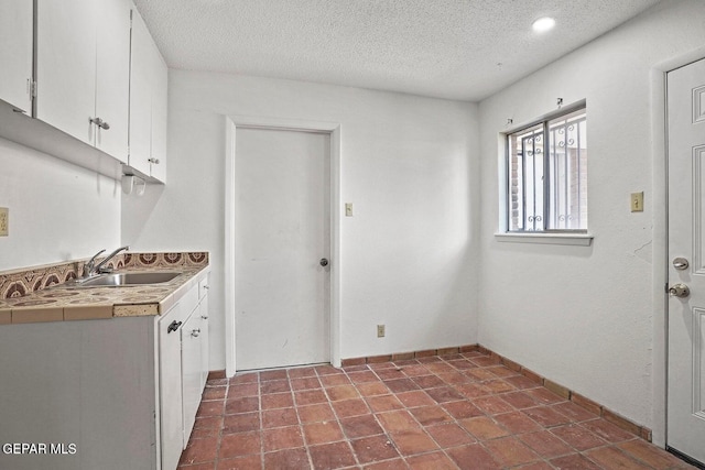 clothes washing area featuring a textured ceiling, a sink, and baseboards