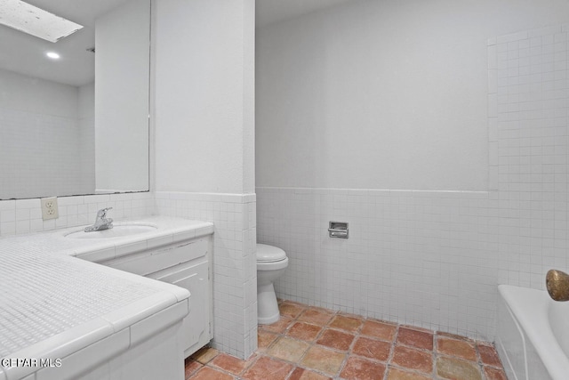 bathroom featuring vanity, a tub, toilet, wainscoting, and tile walls