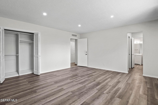 unfurnished bedroom with visible vents, baseboards, a closet, a textured ceiling, and wood finished floors