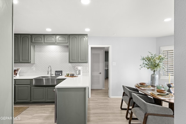 kitchen with gray cabinetry, sink, backsplash, and light wood-type flooring