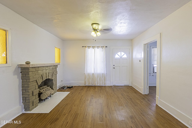 foyer featuring wood-type flooring, a brick fireplace, a textured ceiling, and ceiling fan