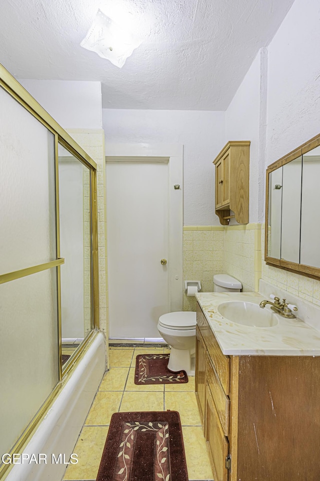 full bathroom with combined bath / shower with glass door, vanity, toilet, tile patterned floors, and a textured ceiling