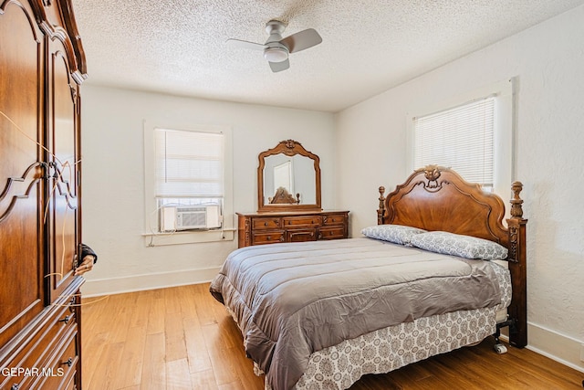 bedroom with cooling unit, a textured ceiling, ceiling fan, and light wood-type flooring