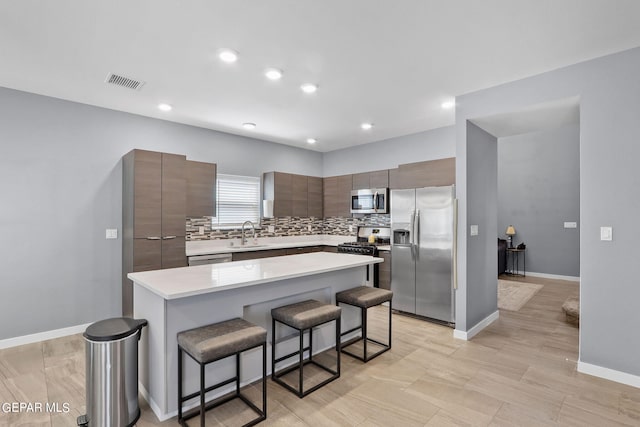 kitchen with sink, a breakfast bar, appliances with stainless steel finishes, backsplash, and a kitchen island