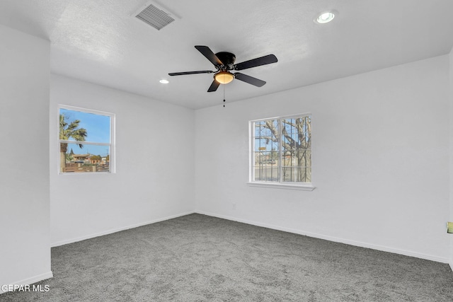 unfurnished room featuring ceiling fan, a healthy amount of sunlight, a textured ceiling, and dark carpet