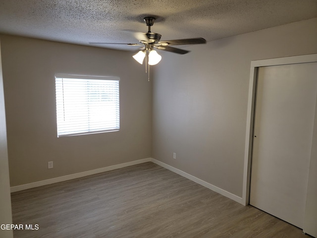 unfurnished bedroom with a textured ceiling, light hardwood / wood-style flooring, a closet, and ceiling fan