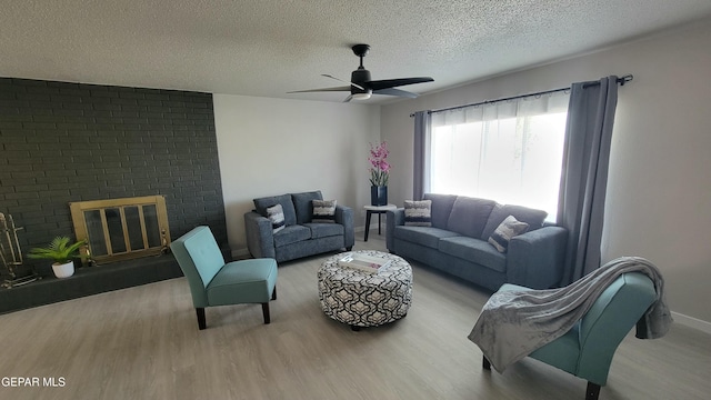 living room featuring ceiling fan, a fireplace, light hardwood / wood-style floors, and a textured ceiling