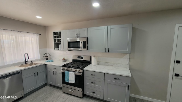 kitchen with appliances with stainless steel finishes, sink, gray cabinetry, backsplash, and light stone counters