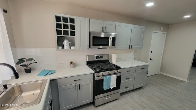 kitchen with appliances with stainless steel finishes, light stone countertops, sink, and gray cabinetry