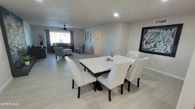 dining space with a brick fireplace, light hardwood / wood-style floors, and a textured ceiling