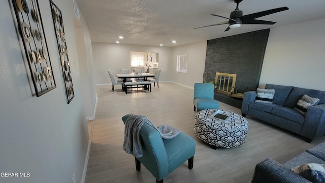 living room featuring ceiling fan, a brick fireplace, a textured ceiling, and light hardwood / wood-style floors