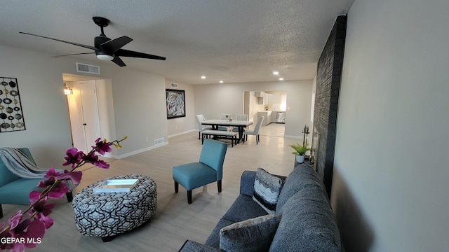 living room featuring ceiling fan, a textured ceiling, and light hardwood / wood-style floors