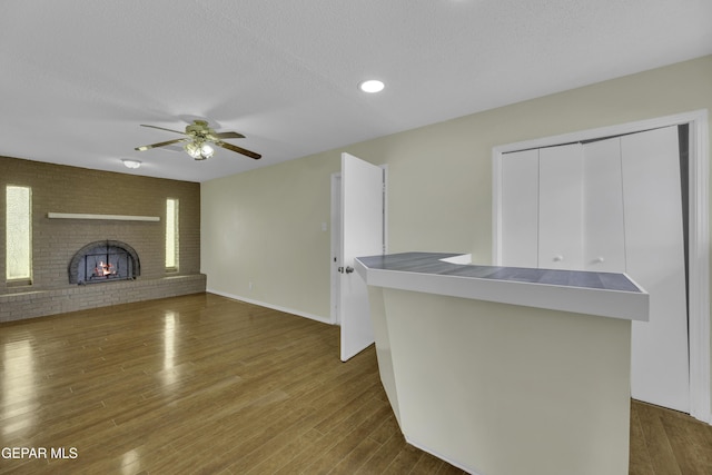 unfurnished living room featuring dark hardwood / wood-style flooring, a brick fireplace, a textured ceiling, and ceiling fan