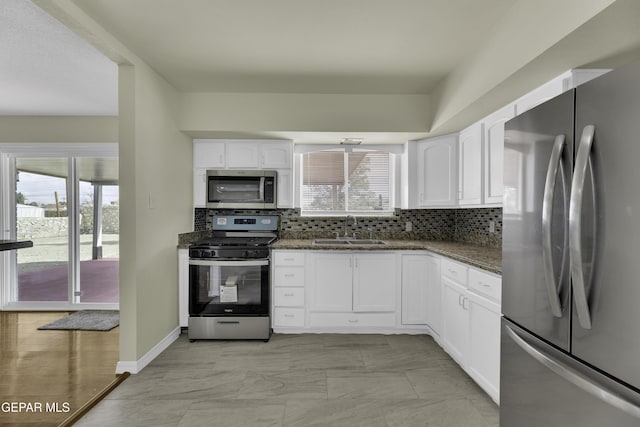 kitchen with white cabinetry, sink, stainless steel appliances, and dark stone countertops