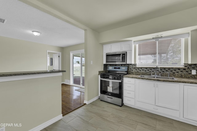 kitchen featuring appliances with stainless steel finishes, sink, white cabinets, and dark stone counters